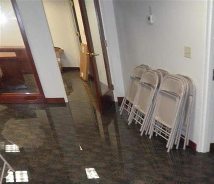 water with ceiling lights reflecting off carpeted office area, folding chairs leaning on wall